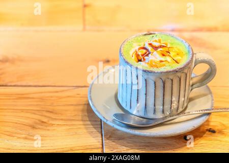 A frothy Japanese matcha green tea latte served in a rustic ceramic cup with a spoon, adorned with whipped cream and a drizzle of caramel, sits inviti Stock Photo