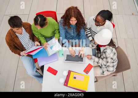 High angle view of a group of multiracial students doing the highschool homework using a laptop to search info. Classmates studying together on the university campus library, learning the lesson. High quality photo Stock Photo