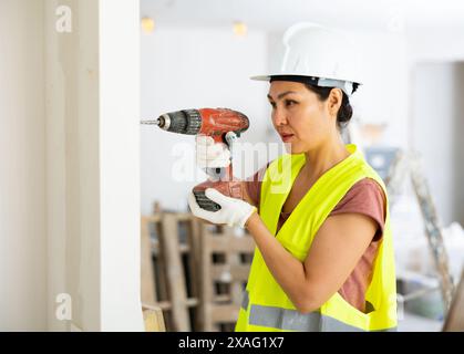 Woman builder using drill to bore hole in wall Stock Photo