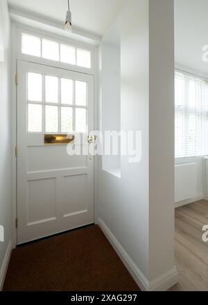 Minimalist, white painted front door and entrance hallway of an Edwardian house converted into flats in north London. Stock Photo