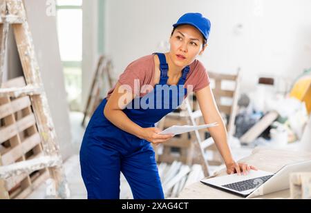 Woman builder checking documentation, using laptop Stock Photo