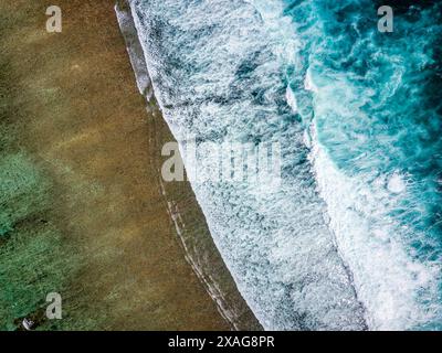 Top down aerial view of ocean waves breaking against a shallow tropical coral reef Stock Photo