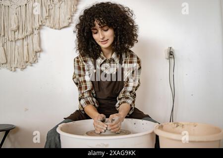Young adult female potter using a pottery wheel to sculpt ceramic dishes in an art studio environment. Stock Photo