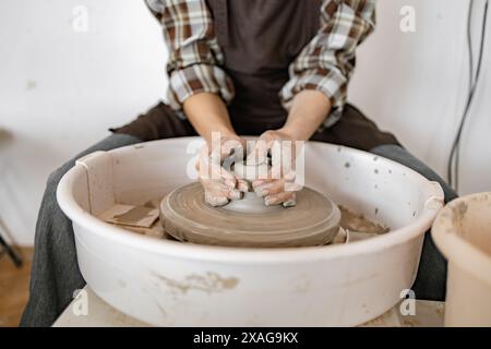Female potter shaping a ceramic dish with potter's wheel in studio. Hands-on creative process, craftsmanship, and artistry. Stock Photo