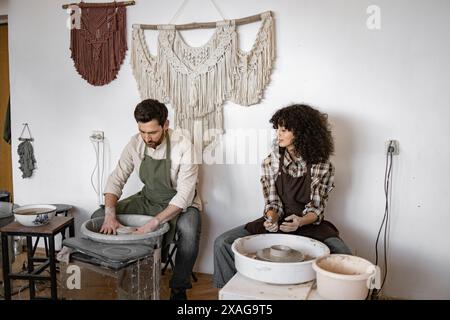 Man and woman potters working together at studio using potter's wheel and creating clay vases. Stock Photo