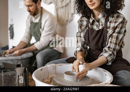Man and woman working together creating pottery using clay on potter's wheel in a studio. Stock Photo