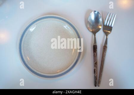 Empty plate with spoon and fork on white table. Top view. Stock Photo