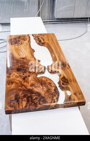 Live edge elm burl slab table top with central epoxy resin river on sawhorses in professional workshop Stock Photo
