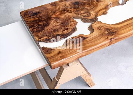Live edge elm burl slab table top with central epoxy resin river on sawhorses in professional workshop Stock Photo
