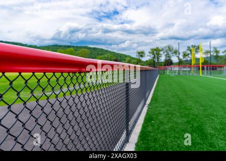 Black chain link fence with red fence cap and softball / baseball sports field in background. Stock Photo