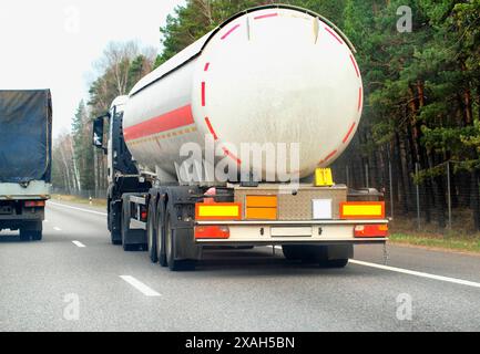 A truck with a semi-trailer tanker transports a dangerous chemical cargo of acid and alkali along a country road in the spring. Stock Photo