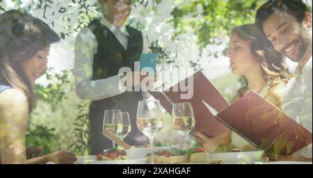 Image of foliage over caucasian friends and waitress ordering wine at restaurant Stock Photo