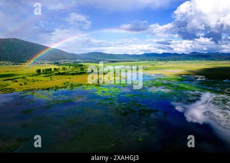 Rainbow over lake Cerknica, the largest intermittent lake in all of Europe, surrounded with lush forest and beautiful mountains, Slovenia Stock Photo