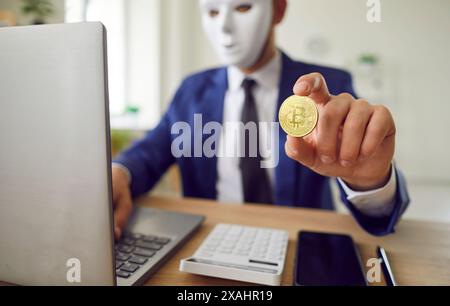 Anonymous Man In Mask Holding Bitcoin Coin And Working On Laptop Stock Photo