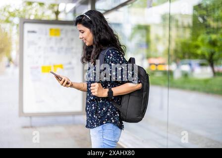 Young woman using smart phone at the bus stop in the city Stock Photo