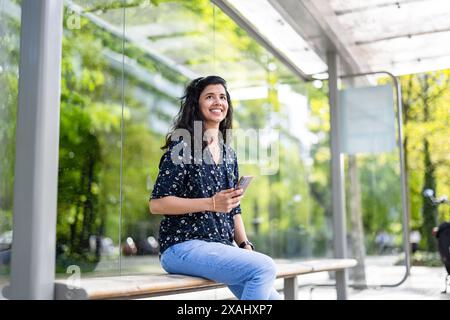 Young woman using smart phone at the bus stop in the city Stock Photo
