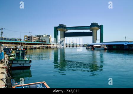 Samcheok City, South Korea - May 18, 2024: The Tsunami Safety Tower stands prominently at the entrance of Samcheok Port, with fishing boats docked nea Stock Photo