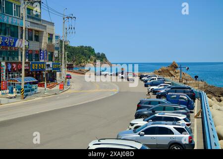 Samcheok City, South Korea - May 18th, 2024: A view towards Lion Rock from Isabu Plaza, showcasing the coastal road lined with parked cars and local s Stock Photo