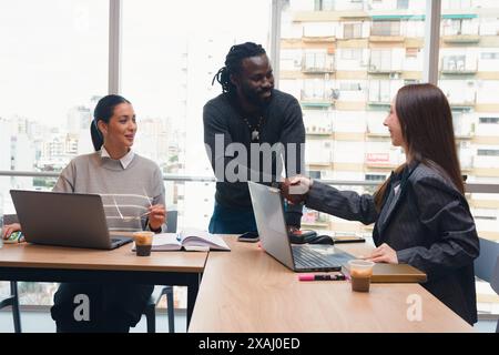 Young Woman and African Man shaking hands celebrating a new affiliation and closing a deal. There is another woman sitting next to witnessing the nego Stock Photo