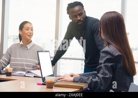 An African Man standing with hands on the table and other Woman sitting are meeting discussing with another Woman who has a laptop and is writing down Stock Photo