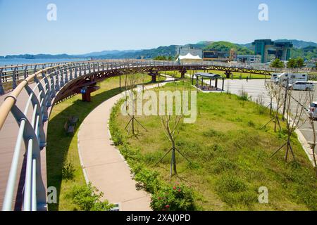 Samcheok City, South Korea - May 18th, 2024: An elevated view of the walkway and green space at Isabu Plaza. The curved pedestrian bridge overlooks th Stock Photo