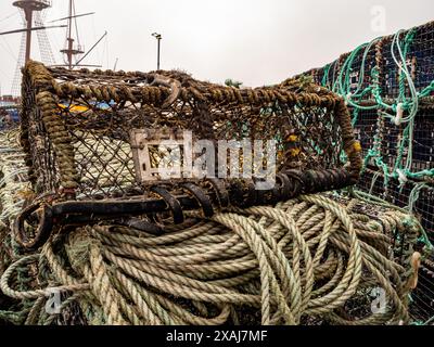 A lobster pot sat on top of a rope bundle in the marina at Whitby. Masts of the Endeavour are in the background on a very misty day. Stock Photo