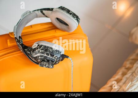 A pair of camouflage-patterned headphones resting on a yellow suitcase. The suitcase is placed on a tiled floor. Stock Photo