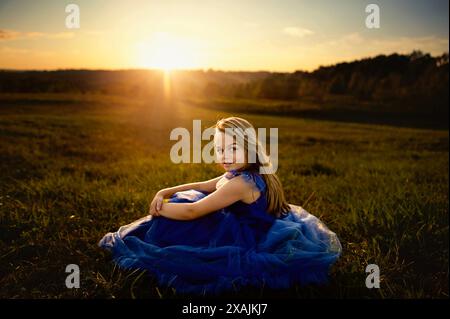 Portrait beautiful tween sitting in open field at sunset Stock Photo