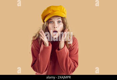 Portrait of young woman in yellow hat and red sweatshirt with surprised face looking at camera. Stock Photo