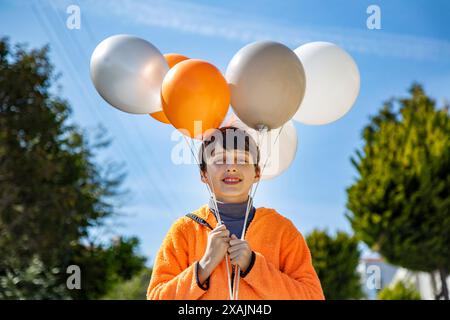 happy boy with colorful balloons on the head against blue sky Stock Photo