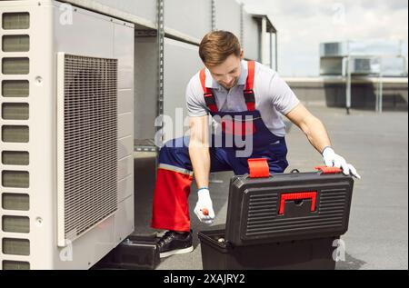 Technician or electrical engineer in uniform installing air conditioner sitting on the roof Stock Photo