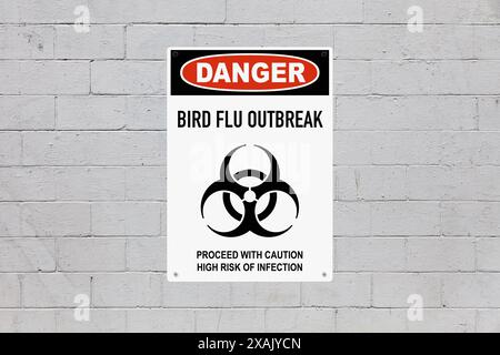 Black, red and white danger sign attached on a brick wall painted in grey. The sign stating “Danger - Bird Flu outbreak - Proceed with caution, high r Stock Photo