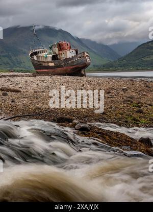 Corpach shipwreck stranded on shore near Fort William, between mountains and a river, in the west coast of Scotland. Vertical Stock Photo