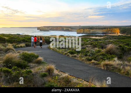 Young tourists walking on a trail facing the Baker's Oven offshore rock formation along the coast of the Tasman Sea in the Twelve Apostles Marine Nati Stock Photo