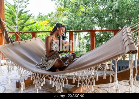 North America, Caribbean, Hispaniola Island, Dominican Republic, Samana Peninsula, Sanchez, Jardines La Loma, Pretty dark-skinned Latina sits in a hammock and drinks from a coconut Stock Photo