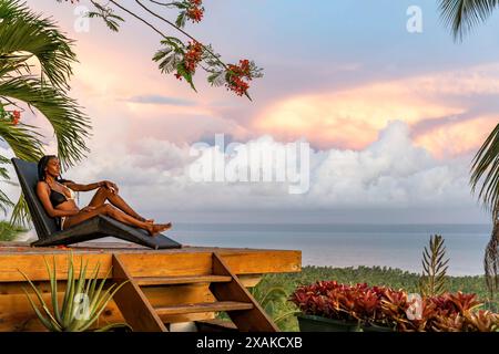 North America, Caribbean, Hispaniola Island, Dominican Republic, Samana Peninsula, Sanchez, Jardines La Loma, Attractive dark-skinned Latina in bikini lying on a sun lounger overlooking the bay of Samana Stock Photo