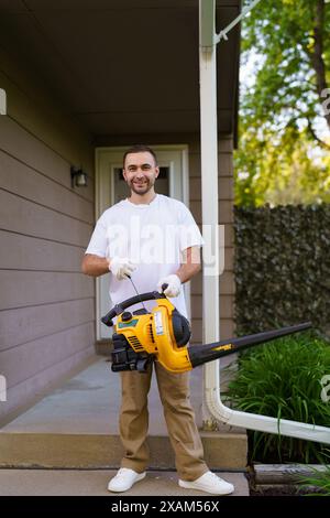 Gardener clearing up the leaves using a leaf blower tool Stock Photo