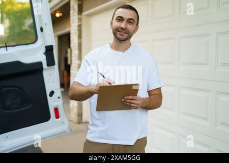 Courier with clipboard near delivery van outdoors Stock Photo