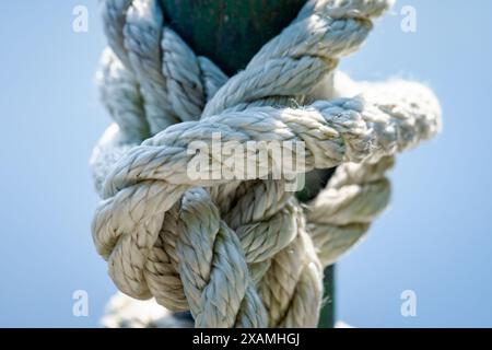 Close up of weathered rope tied into a knot around a metal pole. Stock Photo