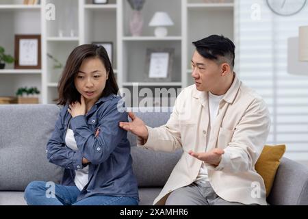 Asian couple having a serious conversation on the couch, capturing emotions of disagreement, concern, and relationship issues in a modern living room setting. Stock Photo