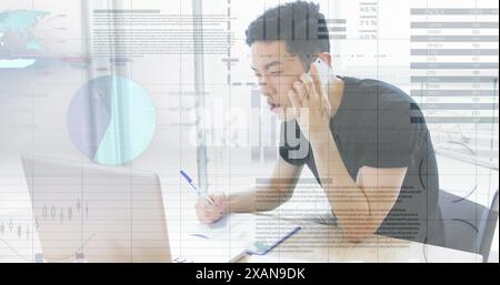 Image of financial data processing over asian businessman using laptop and smartphone at office Stock Photo