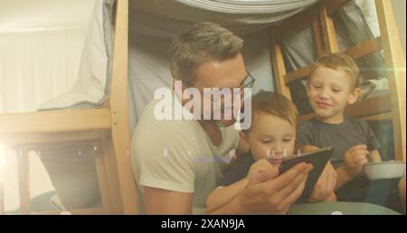 Image of light spots over happy caucasian father using tablet with sons Stock Photo