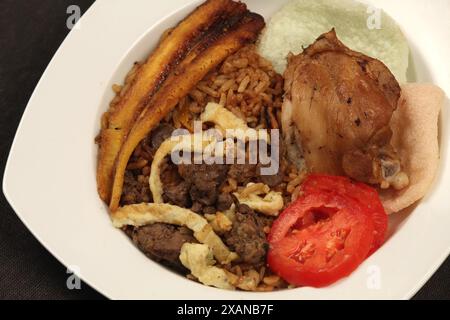 Plate with delicious nasi goreng, krupuk fried plantain, egg, sliced tomato and chicken liver sambal. Stock Photo