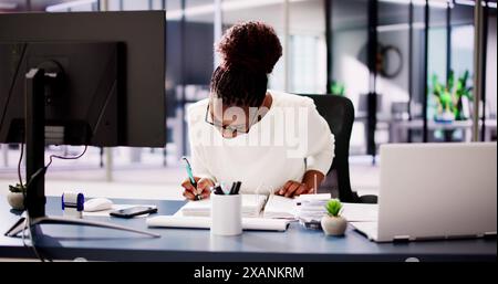 Successful African American Accountant Woman Smiling While Using Calculator At Her Desk In Busy Office Setting Stock Photo