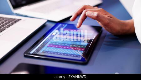 Analyzing Financial Charts on a Tablet in the Workplace: An African American Data Analyst Reports on Virtual Accounts. Stock Photo