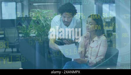 Image of stock market data processing over diverse male and female colleagues discussing Stock Photo