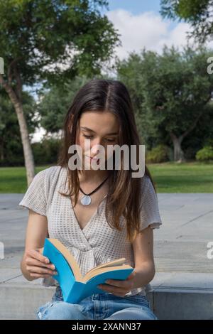 College girl very focused reading a book on campus. Academic life, education, relaxation, break, student on the grass Stock Photo