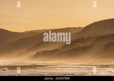 Distant view sea mist covering a hilly coastline in golden light at Fairhaven on the The Great Ocean Road in Victoria, Australia Stock Photo