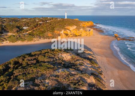 Aerial view of a wide sandy beach below a distant lighthouse perched on a cliff top at Aireys Inlet on the The Great Ocean Road in Victoria, Australia Stock Photo