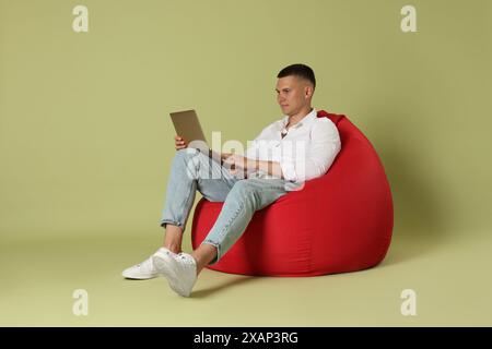 Handsome man with laptop on red bean bag chair against green background Stock Photo